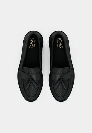 Para czarnych plecionych skórzanych mokasynów z frędzlami, firmowymi wkładkami z napisem "TOMS Wear Good", prezentowana na białym tle.