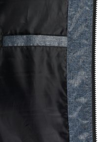 Svart interiørstoff med en lomme i denim-mønster. Lommen har en synlig søm og kontrast mellom teksturer og farger.