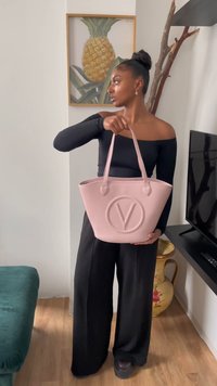 Roza torba iz teksturiranega materiala, ki ima prominentno reliefno 'V' logo. Ima dva dolga ročaja in širok odprtina.