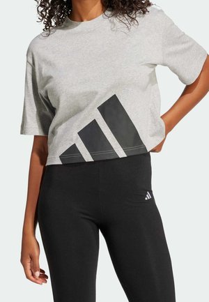 Camiseta gris corta con diseño geométrico negro que presenta tres rayas anguladas. Combinada con leggings negros, que muestran un look elegante y ajustado.