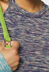 En person som bär en flerfärgad ribbad ärmlös topp och har ett limegrönt väskrem över axeln.