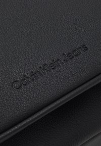 Czarna torba ze skóry o teksturowej fakturze z wytłoczonym logo "Calvin Klein Jeans". Minimalistyczny design z gładkimi krawędziami. Trwałe, eleganckie wykończenie.