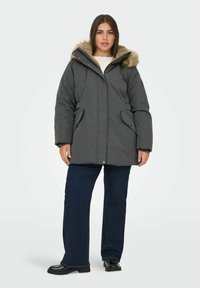 Pelēks puffa mētelis ar mākslīgās kažokādas odere kapuci, priekšā ar rāvējslēdzēju, sānu kabatām un elastīgiem piedurkņu galiem. Modelis valkā tumšzilas platās bikses.