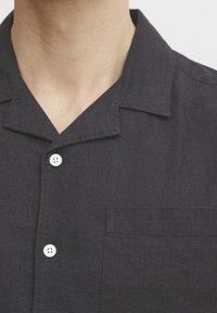 Chemise à manches courtes en lin foncé avec col, dotée d'une poche plaquée et de boutons blancs, tissu texturé avec un motif subtil.