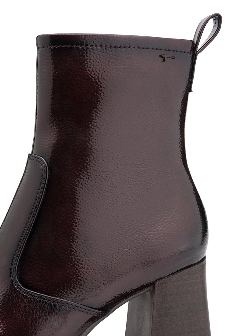 Stivaletto in pelle bordeaux con finitura lucida, caratterizzato da un design senza cuciture, punta arrotondata e tacco alto a strati. Accentuato da un'asola per il tiro.