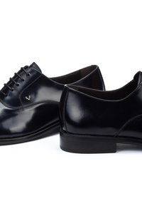 Shiny black leather men's dress shoes with laces, low heels, and detailed stitching on white background.