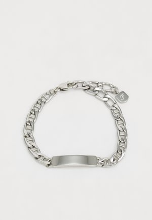 Pulsera de metal plateado con eslabones de cadena entrelazados, una placa central lisa y una pequeña etiqueta de marca. Diseño duradero y elegante.