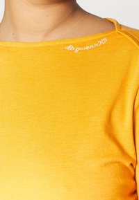 T-shirt di cotone giallo con scollo a barca, con testo ricamato bianco "dogwear♥" vicino alla spalla. Texture morbida, design aderente.