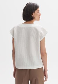 Witte top met korte mouwen in een gestructureerd wafelbreipatroon, met een losse pasvorm en ronde halslijn, gecombineerd met bruine hoge taillebroek.