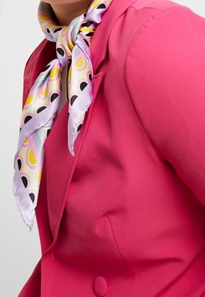 Personne portant un blazer rose vif et une écharpe en soie pastel avec un motif géométrique jaune, noir et rose nouée autour du cou.