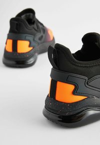 Baskets de sport noires et orange avec une tige texturée, un col rembourré, des accents réfléchissants et une semelle noire à motifs.