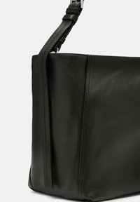Czarna skórzana torebka o gładkiej teksturze, charakteryzująca się usztywnionym kształtem, regulowanym paskiem oraz starannym przeszyciem wzdłuż szwów.