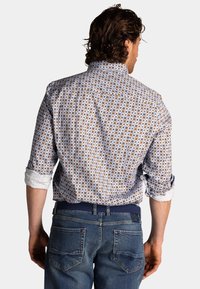 Witte shirt met een patroon van bruine en blauwe cirkels, gedragen met opgerolde mouwen, in combinatie met blauwe denim jeans.