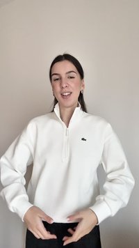 Biela mikina so zipsom a dlhými rukávmi, s malým zeleným logom krokodíla na ľavej strane hrude. Hladká bavlnená látka, voľný strih.