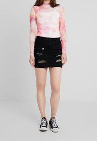 Haut à manches longues tie-dye rose et blanc, associé à une mini-jupe en denim noir avec des détails déchirés et un ourlet effiloché. Baskets noires.