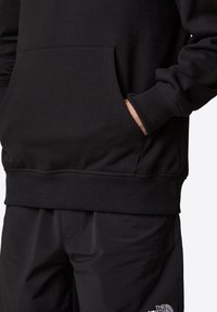 Svart sweatshirt med känguruficka, ribbad mudd och nederkant. Tillverkad av mjukt tyg, med en subtil logotyp på nedre högra sidan.