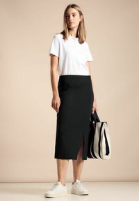 Polo bianco, gonna a tubino nera con spacco laterale, sneakers bianche e borsa a tracolla a righe bianco e nere. Tessuto morbido e design aderente.