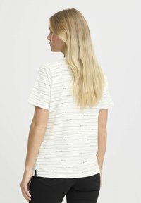 Hvid kortærmet T-shirt med sorte vandrette striber, der viser navne på byer; afslappet pasform med rund nederkant og sidesprækker.