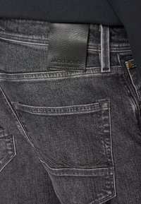 Črne denim hlače s teksturirano površino, ki imajo usnjen obliž z oznako "JACK & JONES" in standardne zadnje žepe.