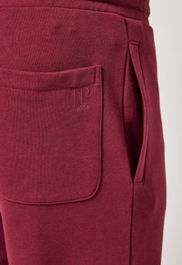 Burgundy joggers i mjukt tyg, med en stor fackficka med präglad logodetalj och en avsmalnad passform för komfort.