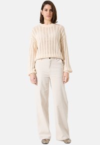 Pull en tricot crème avec des motifs ouverts verticaux, associé à un pantalon en velours côtelé beige à jambes larges et des ballerines métalliques. Design simple et décontracté.