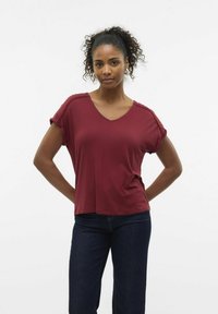 T-shirt burdeos de manga corta y escote en V, fabricado en tejido suave, con mangas enrolladas y un ajuste relajado, combinado con vaqueros oscuros.