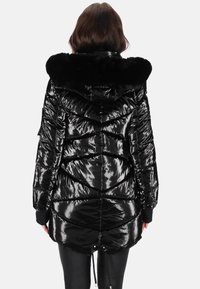 Fekete párnázott dzseki fényes, steppelt felülettel és műszőrme gallérral. Derékrészen összeszűkített, bordázott mandzsettákkal, amelyek hangsúlyozzák a modern kialakítást.