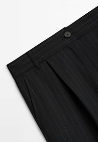 Svart randig byxor i vävt tyg, med knappstängning, veck och subtila gyllene trådar i randmönstret.