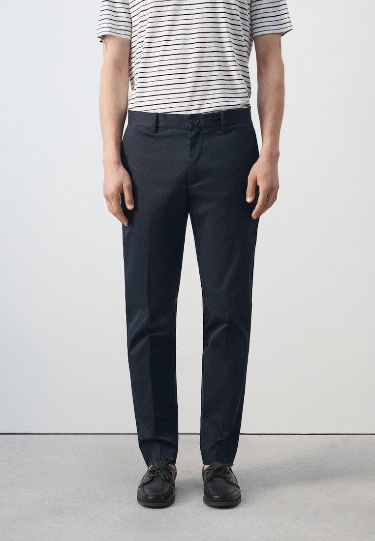 Personne portant un pantalon noir slim, des chaussures noires à lacets, et une chemise blanche à manches courtes avec de fines rayures horizontales noires.