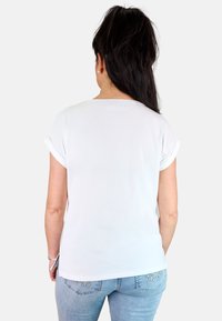 Camiseta blanca de manga corta con puños doblados, escote redondo y textura suave, combinada con jeans de color azul claro con detalles decorativos.