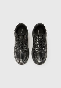 Melnas sporta kurpes ar spīdīgu lakādu apdari, apaļu purngala formu, auklām aiztaisāmu dizainu un teksturētu gumijas zolīti; papēdī ir dekoratīvi elementi.