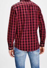 Red and black checked flannel shirt with a folded collar, button closures, and long sleeves, paired with light blue jeans.