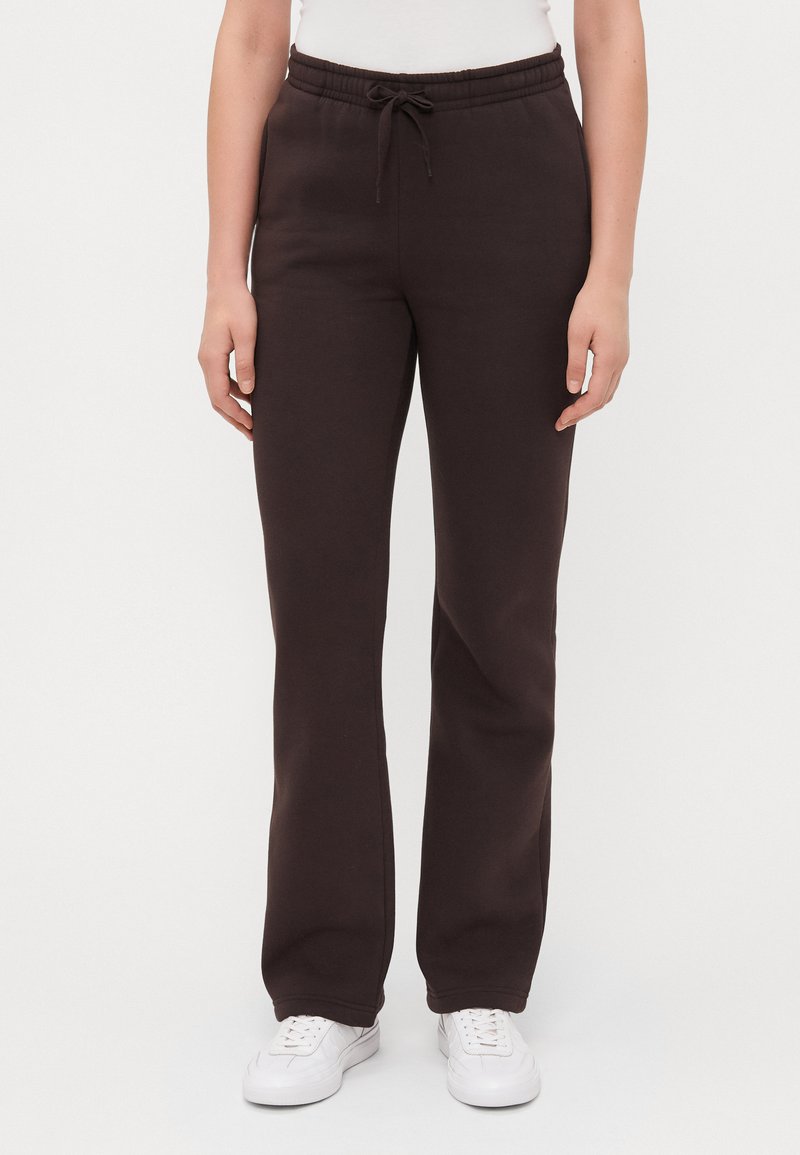 Calças de moletom castanhas com um cós elástico, cordão de ajuste e design de perna reta, feitas de material de algodão suave. Usadas com ténis brancos.