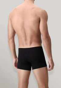 Boxer neri con vestibilità aderente, realizzati in tessuto liscio, con una fascia in vita di altezza media. Schiena e parte superiore del corpo visibili.
