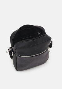 Black crossbody bag with smooth leather and textured accents, featuring a zippered main compartment, front pocket, and adjustable strap.