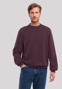 Maroon sweatshirt with a round neckline, long sleeves, and ribbed cuffs. Paired with blue denim jeans. Neutral background.