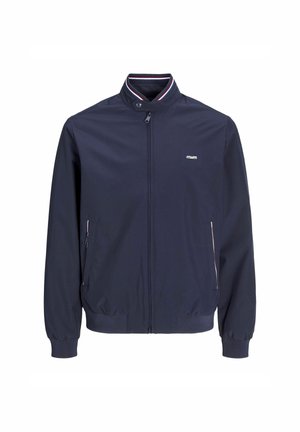 Tumesinise kerge jope kõrge kraega, lukuga ja soonikkoes varrukatega. Omab küljetaskuid kontrastsete ääristega ja logo detailiga.