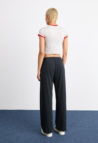 White cropped t-shirt with red trim paired with black wide-leg pants. Soft fabric, relaxed fit. Shoes are light-colored casual sneakers.