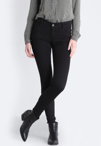 Svarta slim fit-jeans i ett slätt, stretchigt material. Kombineras med en olivgrön blus med knappar och lång ärm samt svarta ankelstövlar.