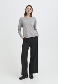 Chemise grise à manches longues avec col rond, associée à un pantalon large noir et des bottines noires. Tissu lisse avec une coupe décontractée.