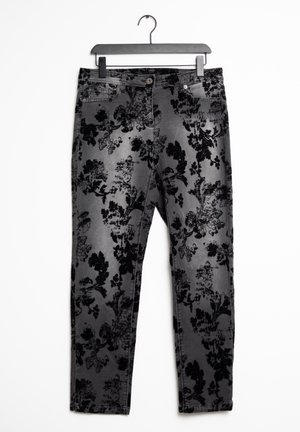 Pantalon en denim gris avec motif floral en velours noir, bouton à l'avant et poches, suspendu à un cintre noir sur fond blanc.