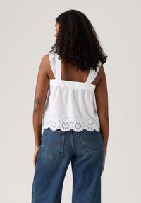 Hvit bomullstopp med blonder i kant, rynkede stropper og firkantet ryggdesign, kombinert med løse mørke denimjeans.