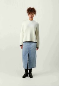 Cream, ribbed sweater with a round neck and black hem, paired with a light blue denim skirt featuring a front slit. Black ankle boots complete the look.