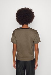 Brun kortärmad t-shirt med en texturerad herringbone-mönster och svart ringning. Baksidan har en avslappnad passform och subtila axeldetaljer.