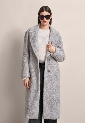 Gray, fluffy coat with a textured surface, open front, large collar, and two buttons. Worn over a light sweater and dark pants.