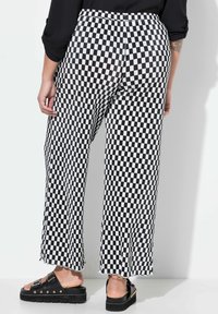 Pantalons à carreaux noir et blanc avec une coupe large, texture côtelée et ourlet effiloché. Associés à des sandales noires épaisses.