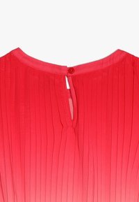 Punainen laskostettu kangas takana olevalla avonaisella aukolla. Pyöreä pääntie, viimeistelty napilla. Pehmeä koostumus ja sileä pinta.