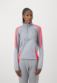 Pullover sportivo grigio chiaro con colletto zip, caratterizzato da strisce rosa brillante sulle spalle e sui pannelli laterali, tessuto leggermente testurizzato.