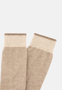 Mangas de pierna beige con una textura suave, que presentan un puño acanalado en un beige más claro. Diseño simple y alargado con costuras uniformes y sin patrones.