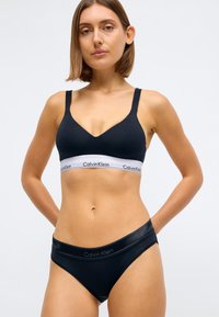 Černá bavlněná podprsenka s nastavitelnými ramínky, designem do V, s bílým elastickým pásem s logem 'Calvin Klein'. Černé kalhotky se shodným brandingem.